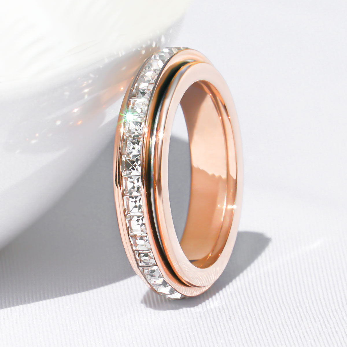 Rose gold crystal fidget ring leaning against the edge of a white bowl on a white background