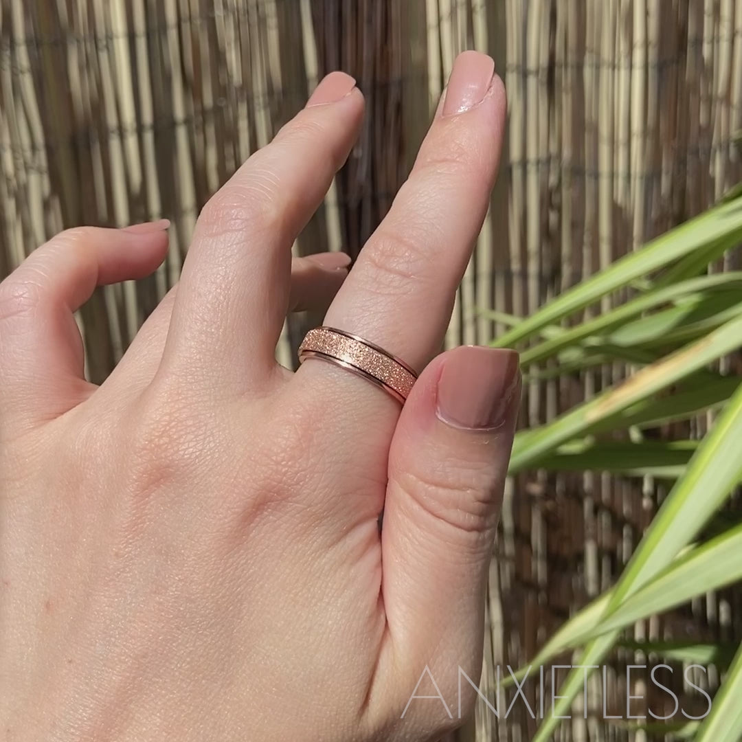 Girl spinning a rose gold anxiety ring on her index finger, set against a backdrop of lush leaves and a bamboo fence