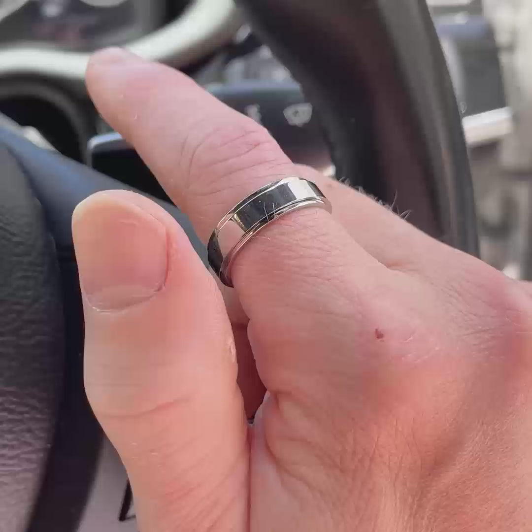 Close-up of a man wearing a silver spinning anxiety ring with a smooth polished design. He demonstrates the ring's spinning motion on a car steering wheel and while walking in the park, wearing a grey shirt