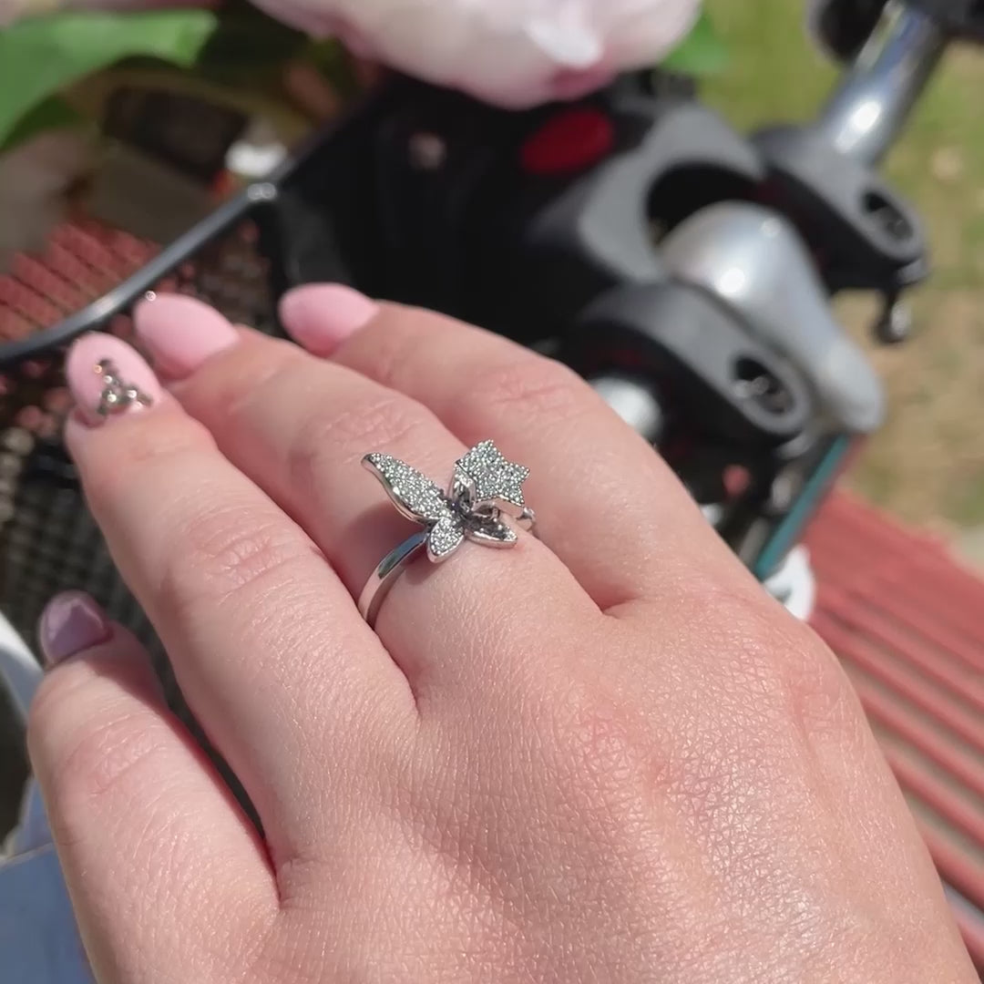 Women spinning silver butterfly fidget ring with star, with background of blue bicycle, black basket, and pink flowers