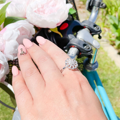 Woman wearing a silver coloured flower fidget ring, with a blue bicycle featuring a black basket adorned with pink flowers in the background