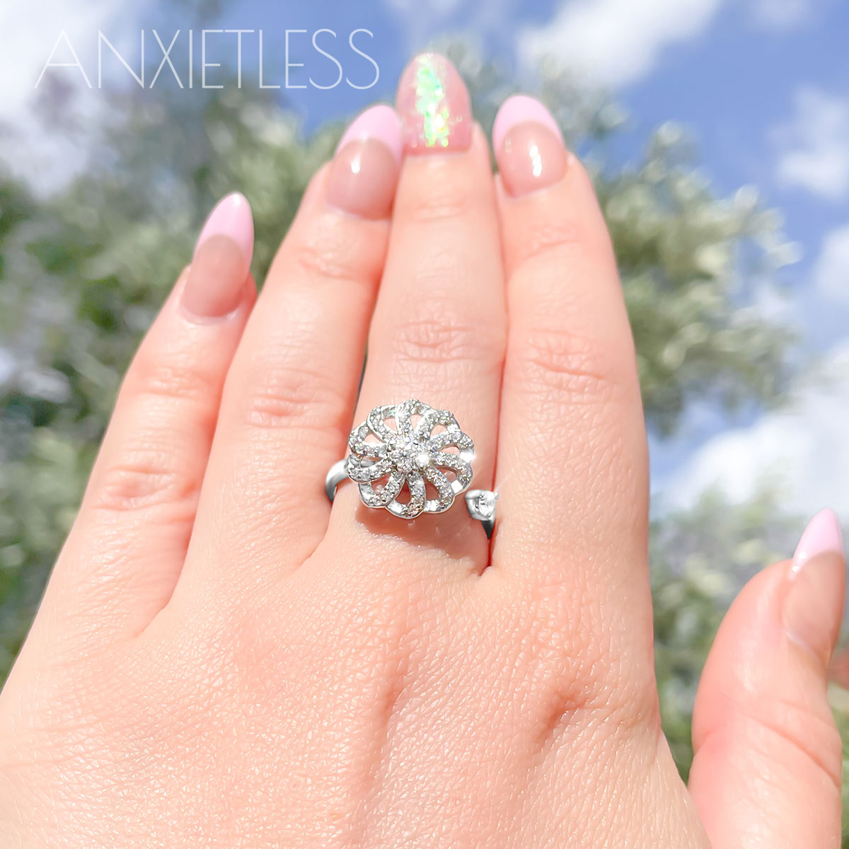 Woman wearing a silver coloured flower fidget ring, with a blurred background of sky and trees
