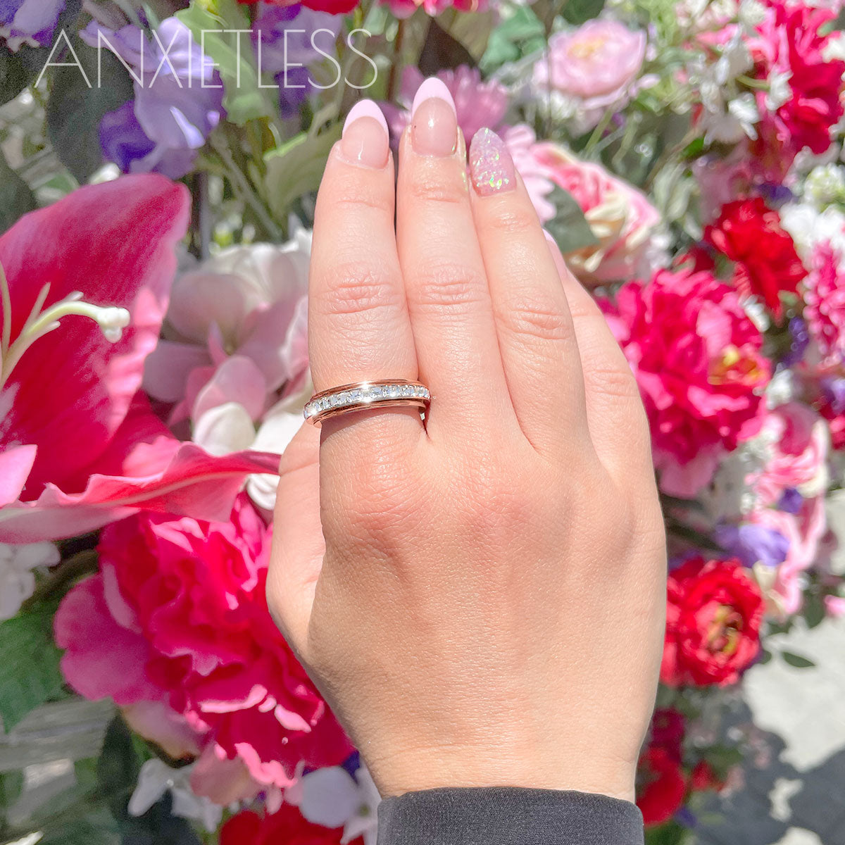 Rose gold crystal fidget ring on index finger with stunning pink, purple, and rose flowers in the background