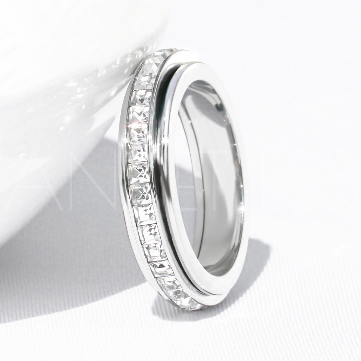 Silver crystal fidget ring leaning against the edge of a white bowl on a white background