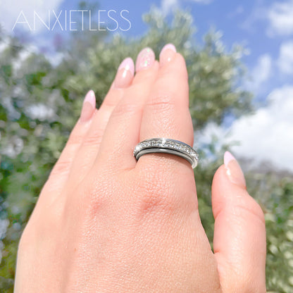 Silver crystal fidget ring worn on index finger, with trees and sky in the background
