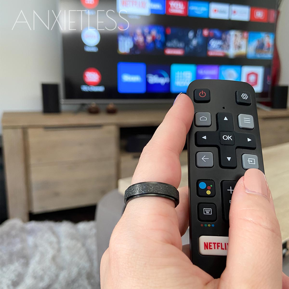 Woman wearing black anxiety ring on index finger, with a TV showing Netflix on the screen, and a TV stand in the background
