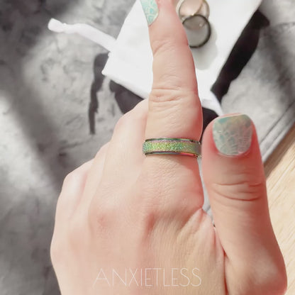 Woman spinning rainbow anxiety ring on index finger. On the background there are brown table, grey table runner, and anxiety rings laid on the white satin bag