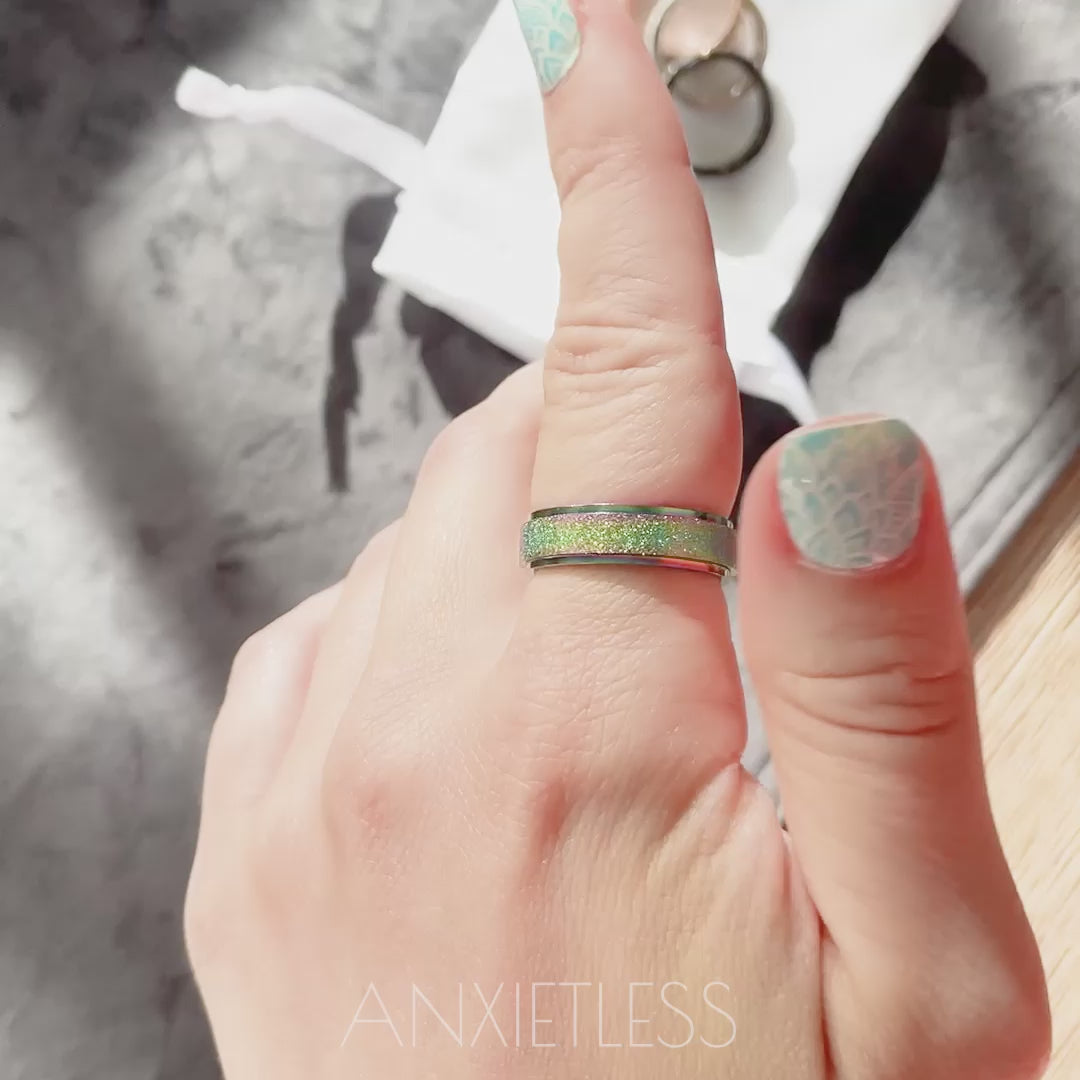 Woman spinning rainbow anxiety ring on index finger. On the background there are brown table, grey table runner, and anxiety rings laid on the white satin bag